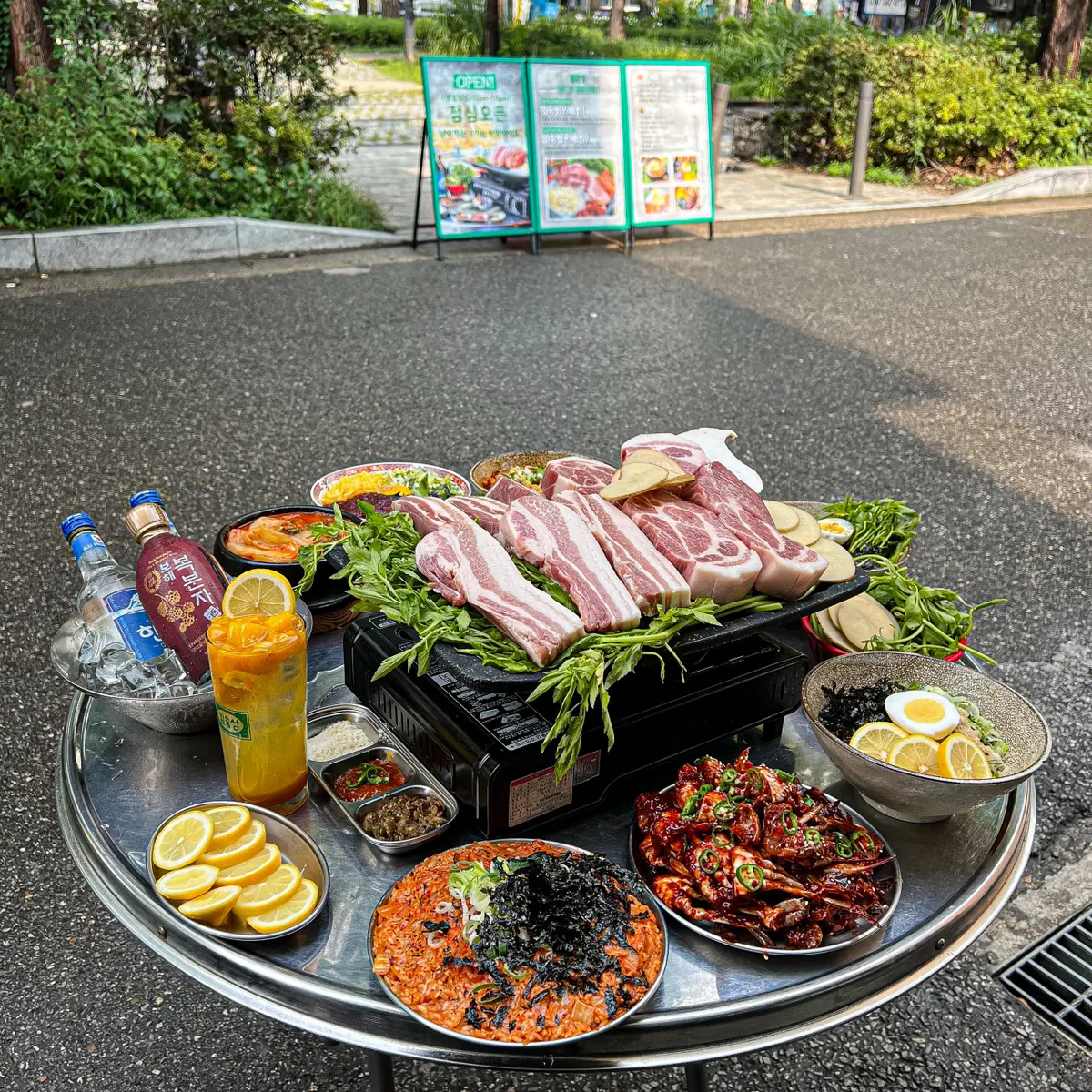 김숙성 이태원점 야외 테이블 한 상 — 불판에 올린 숙성 삼겹살과 미나리, 반찬이 깔린 테이블 · 이태원 맛집 · Itaewon Korean BBQ